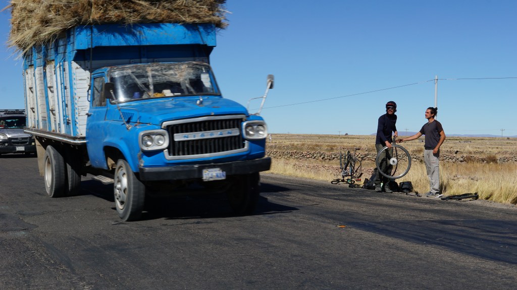 Thomas et son ami en bord de route pour réparer la roue et camion qui passe